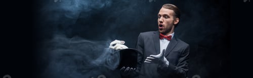 Preview: panoramic shot of shocked magician in suit holding hat with white rabbit, dark room with smoke