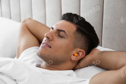 Preview: Man with foam ear plugs sleeping in bed