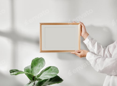 Preview: Hand holding Frame or Poster mock up in living room and window shadow on white wall background.