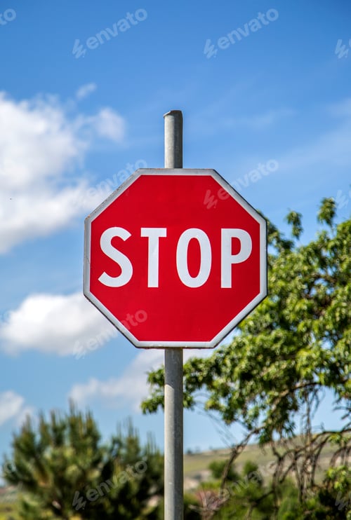Stop Sign Against Blue Sky and Green Trees