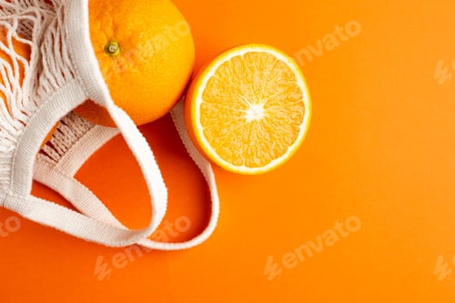 Preview: Cutting orange in cotton shopping eco friendly bag on orange background. Citrus