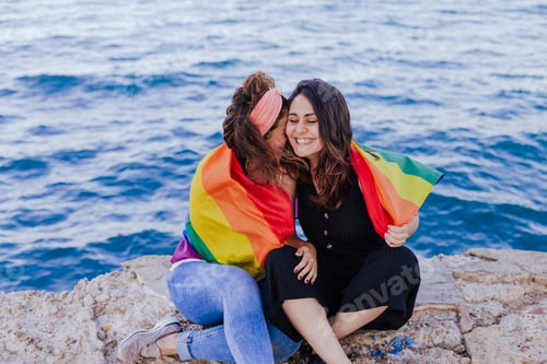 Preview: happy lesbian couple holding rainbow gay flag outdoors. LIFESTYLE and pride concept. love is love