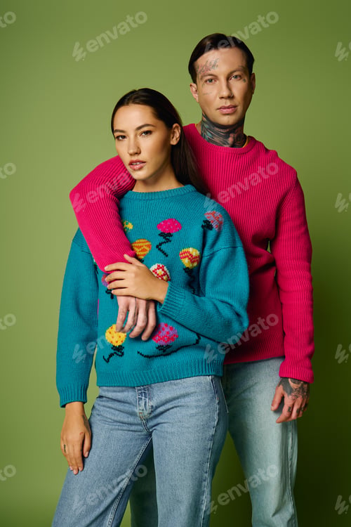 Preview: Stylish young couple poses together in colorful sweaters against a green backdrop