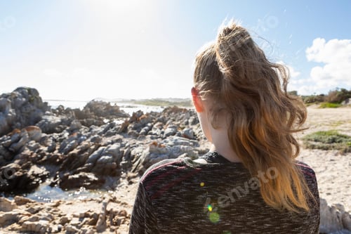 Preview: Teenage girl looking out over a beach and jagged rocks to the ocean
