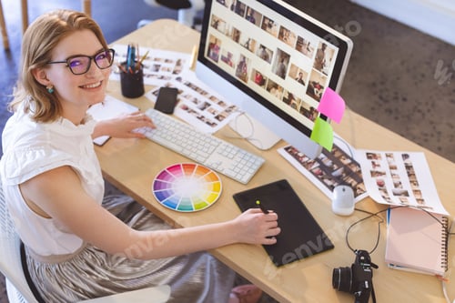 Preview: Young Caucasian female graphic designer working on graphic tablet at desk in office.