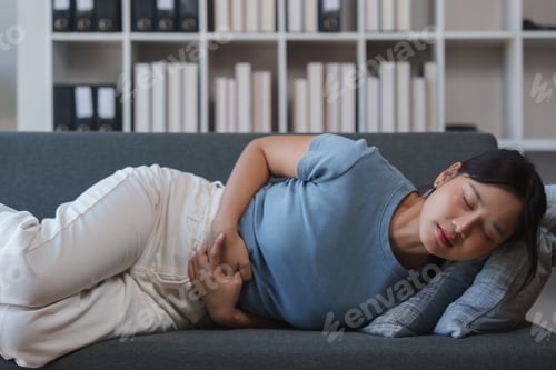 Preview: Young woman suffering from abdominal pain on sofa