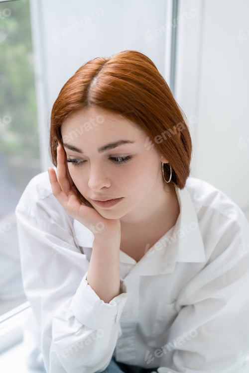 Preview: Displeased redhead woman sitting near window at home