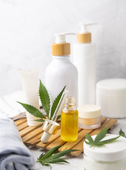 Preview: Dropper bottle with CBD oil near green cannabis leaves near bottles and towel close up