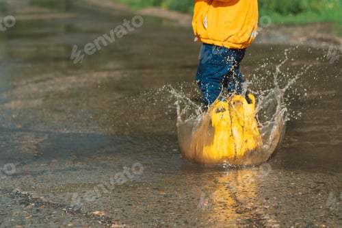 Preview: Child in yellow rubber boots jumping through puddles