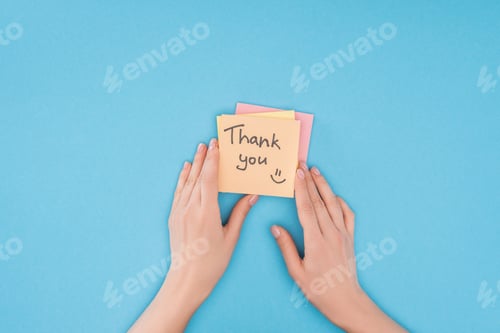 Preview: cropped person holding colorful sticky notes with thank you lettering isolated on blue background