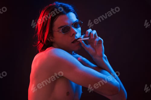 Preview: Holding cigarette. Studio shot in dark studio with neon light. Portrait of serious man