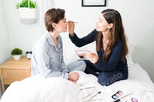 Preview: Side view of a young woman applying makeup to her girlfriend