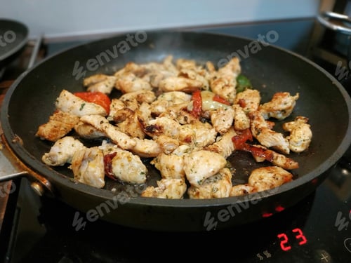 Preview: Closeup shot of chicken breast meat frying with vegies in a black pan on a stove
