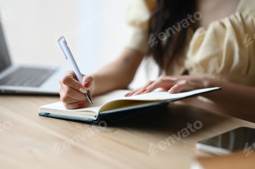Preview: Smiling young woman writing notebook, planning ideas on paper notes at office desk