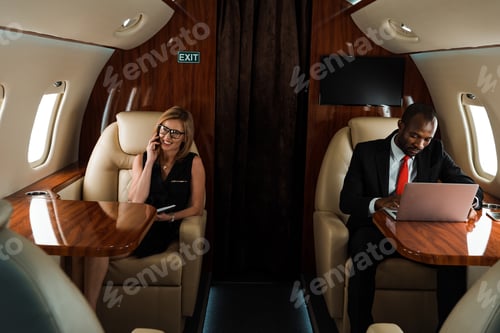 Preview: african american businessman using laptop near businesswoman talking on smartphone in private jet