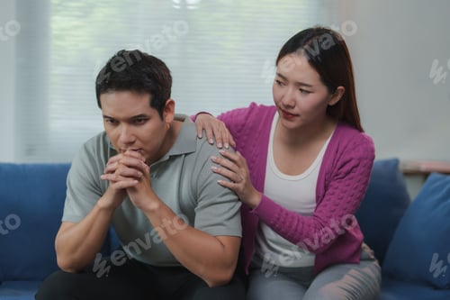 Preview: Young woman comforting her sad husband at home on the sofa