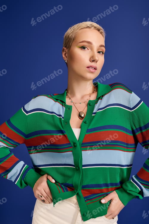 Preview: Fashionable young woman poses confidently against a vibrant blue backdrop in a stylish outfit
