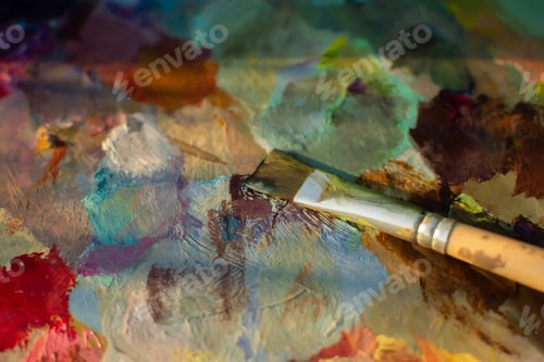 Preview: An artist's palette with an oil paint brush close-up. Blurry multicolored background.