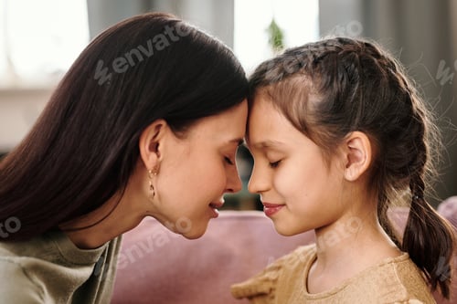 Preview: Side view of young brunette woman and her little daughter touching by foreheads