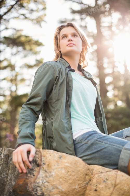 Preview: Young happy jogger sitting on rock and looking away in the nature