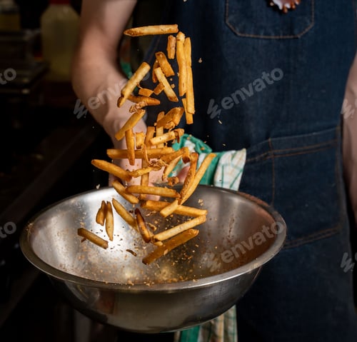 Preview: Person tossing freshly cooked fries with spices on a mixing bowl