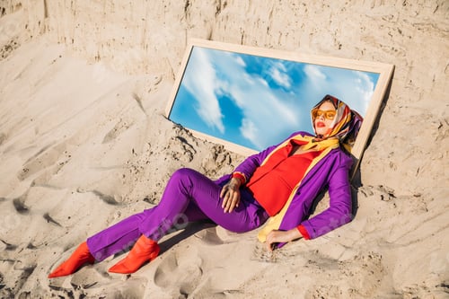 Preview: beautiful model in fashionable clothes lying on mirror with reflection on cloudy sky