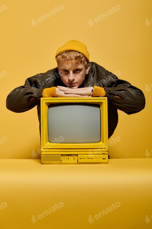 Preview: A fashionable young redhead man showcases his trendy winter outfit leaning on a retro TV