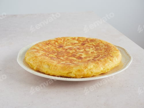 Preview: golden and appetizing whole homemade Spanish potato omelet on a plate on the pink countertop