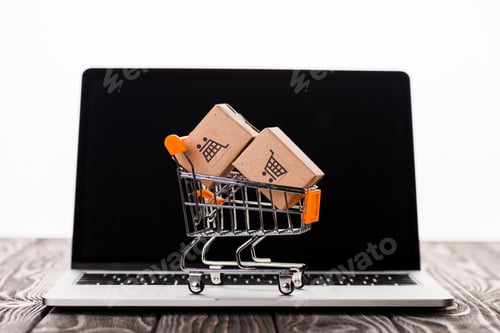 Preview: toy shopping cart with small carton boxes on laptop with blank screen isolated on white, e-commerce