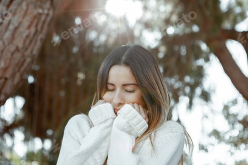 Preview: A millennial girl dressed in a white knitted sweater with her face resting on her hands. Closed eyes