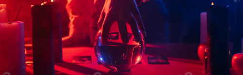 Preview: cropped view of blurred predictor near crystal ball and burning candles on dark background, banner