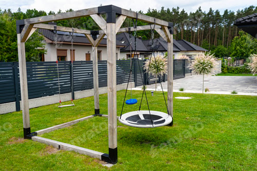 Preview: A modern, square-shaped wooden playground, made of metal corners, standing on the lawn in the yard.