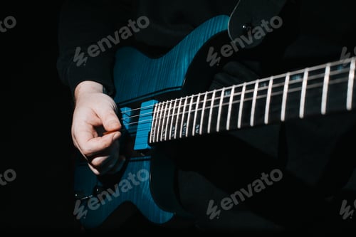 Preview: Close-up musician guitarist playing electric guitar indoors, selective focus on hand with pick