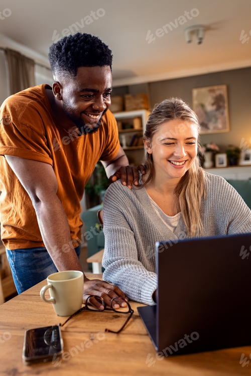 Preview: Smiling young mixed couple using a laptop while working on their home finances.