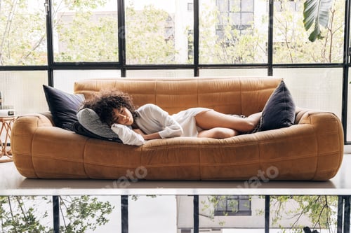 Preview: Pensive young african american woman lying on a yellow sofa in a beautiful loft