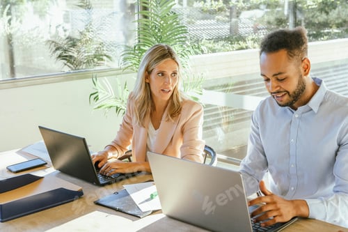 Preview: Two business co-workers talking while working with their computers at the office.