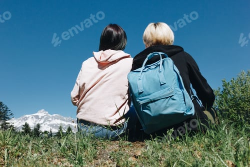 Preview: back view of young female travelers resting on grass in mountains, mont blanc, alps