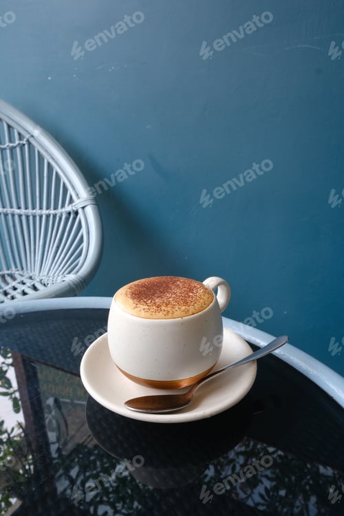 Preview: Cappuccino Cup on Glass Table with White Chair in Background