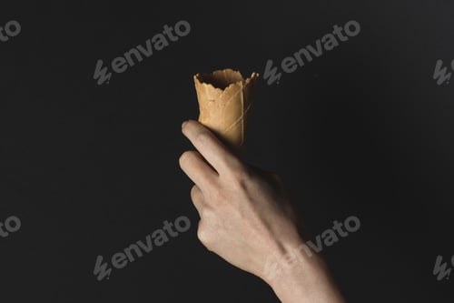 Preview: cropped view of hand holding wafer cone for ice cream, isolated on black