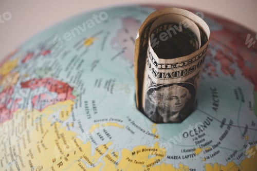 Preview: Closeup shot of a United States dollar bill rolled and put in a hole on top of a globe