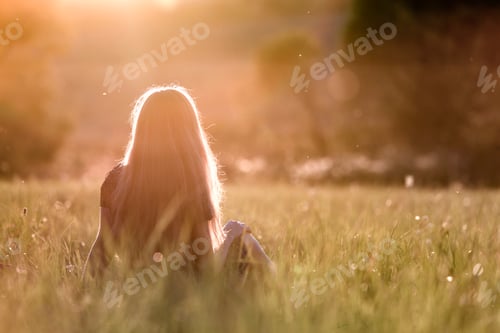 Preview: Back view of a woman with long hair sitting outdoors in sunlight enjoying nature