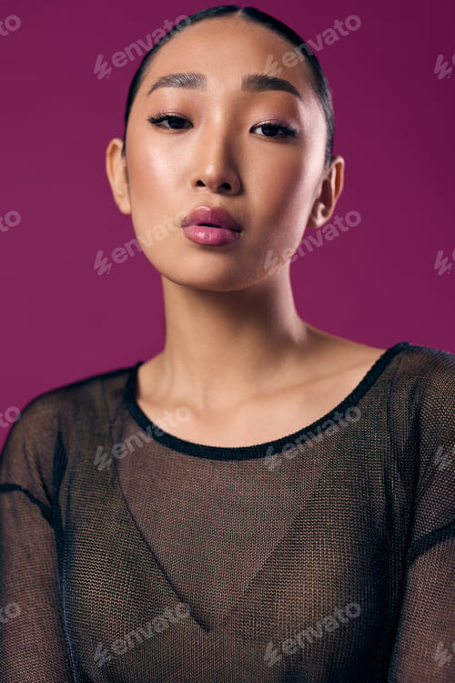 Preview: Fashion asian woman in sheer top posing against purple background with eyes closed and pink lipstick