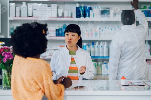 Preview: Japanese woman pharmacist selling drugs to a diverse customers in a pharmacy