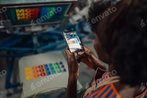 Preview: Close up of interracial printing shop worker taking picture of t-shirt