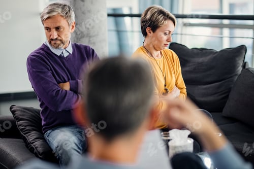 Preview: Displeased couple sitting back to back and ignoring each other during marriage counseling.