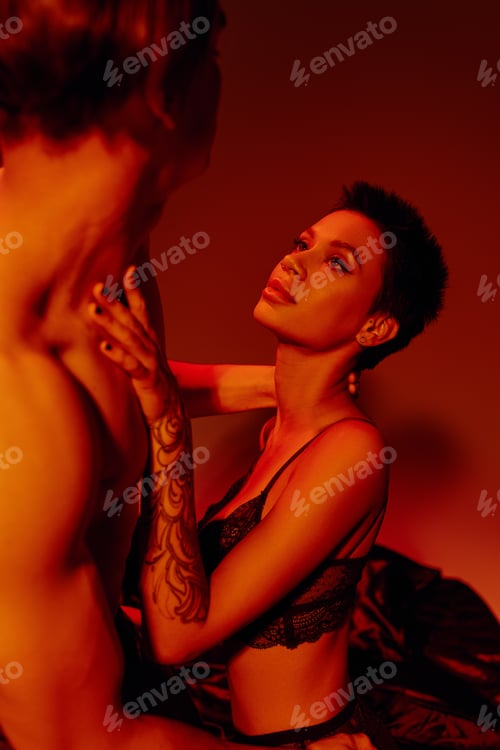 Preview: tattooed woman in black lace bra touching shirtless man on red background