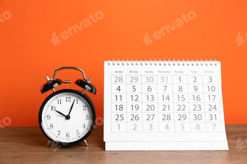 Preview: Calendar and alarm clock on wooden table against orange background
