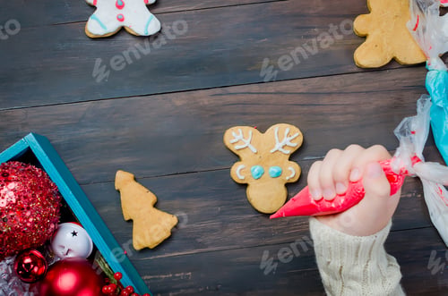 Preview: Happy little girl decorating a christmas gingerbread cookies using colored glazeon wooden table