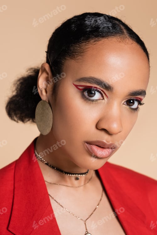 Preview: portrait of stylish african american model in red blazer looking at camera isolated on beige