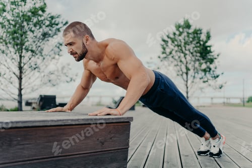 Preview: Confident muscled sportsman in sport wear doing push up outdoors